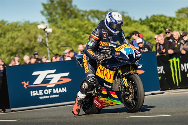 One of the racers on their bike at the Isle of Man TT with a crowd in the distance